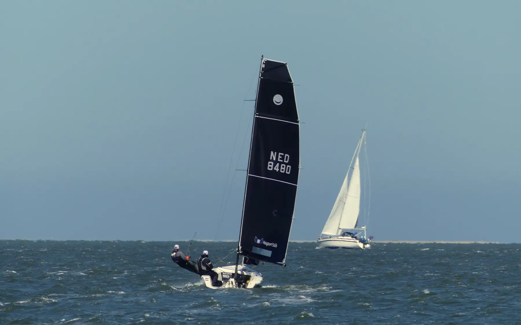 Een zeilboot met een donker grootzeil en een fok op het water