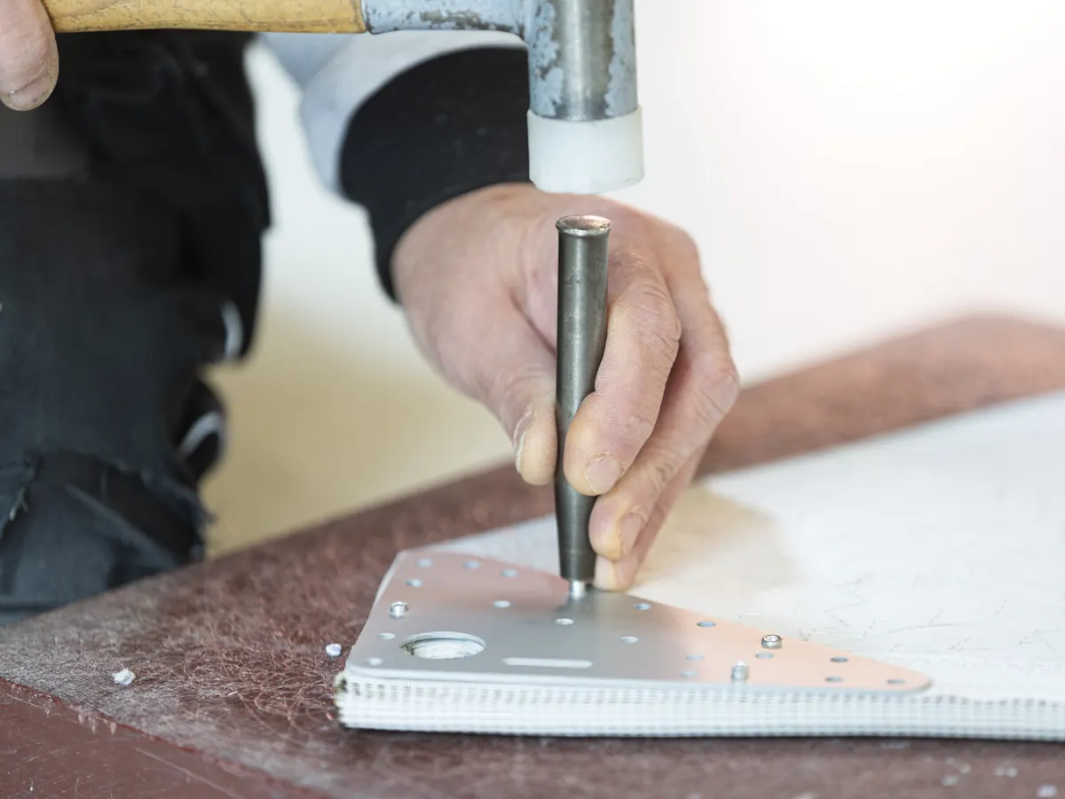 Handwerk aan een zeil met hamer en pons